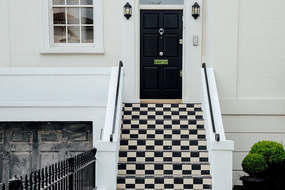 A smart entrance door with a modern black-and-white theme, pitch-black door and black-and-white grid tiles on steps.