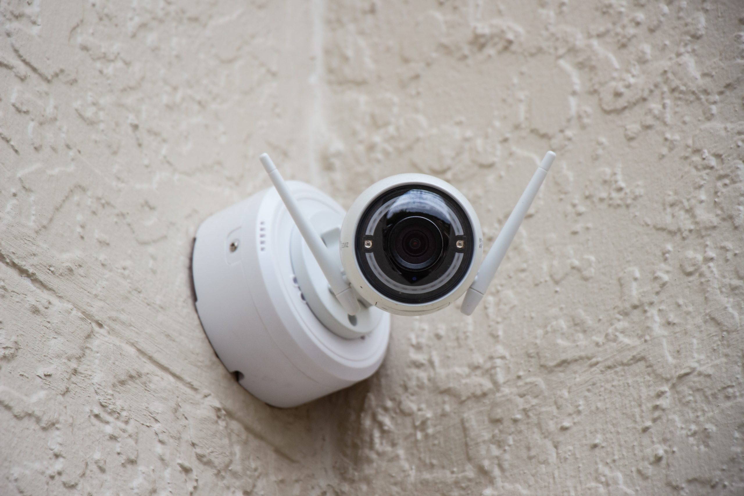 A home surveillance camera attached to the outside corner of a builder pointed towards the viewer.