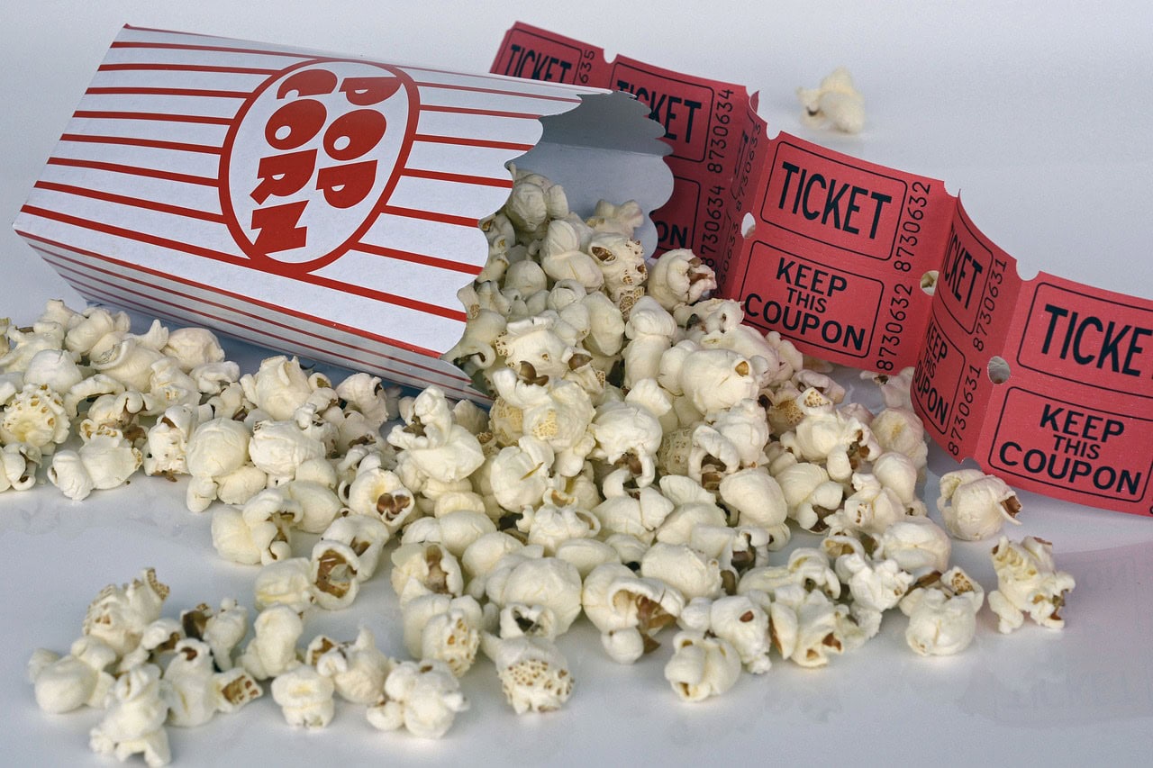 Popcorn and paper tips lie across a clean white table to illustrate movie night ideas at home.